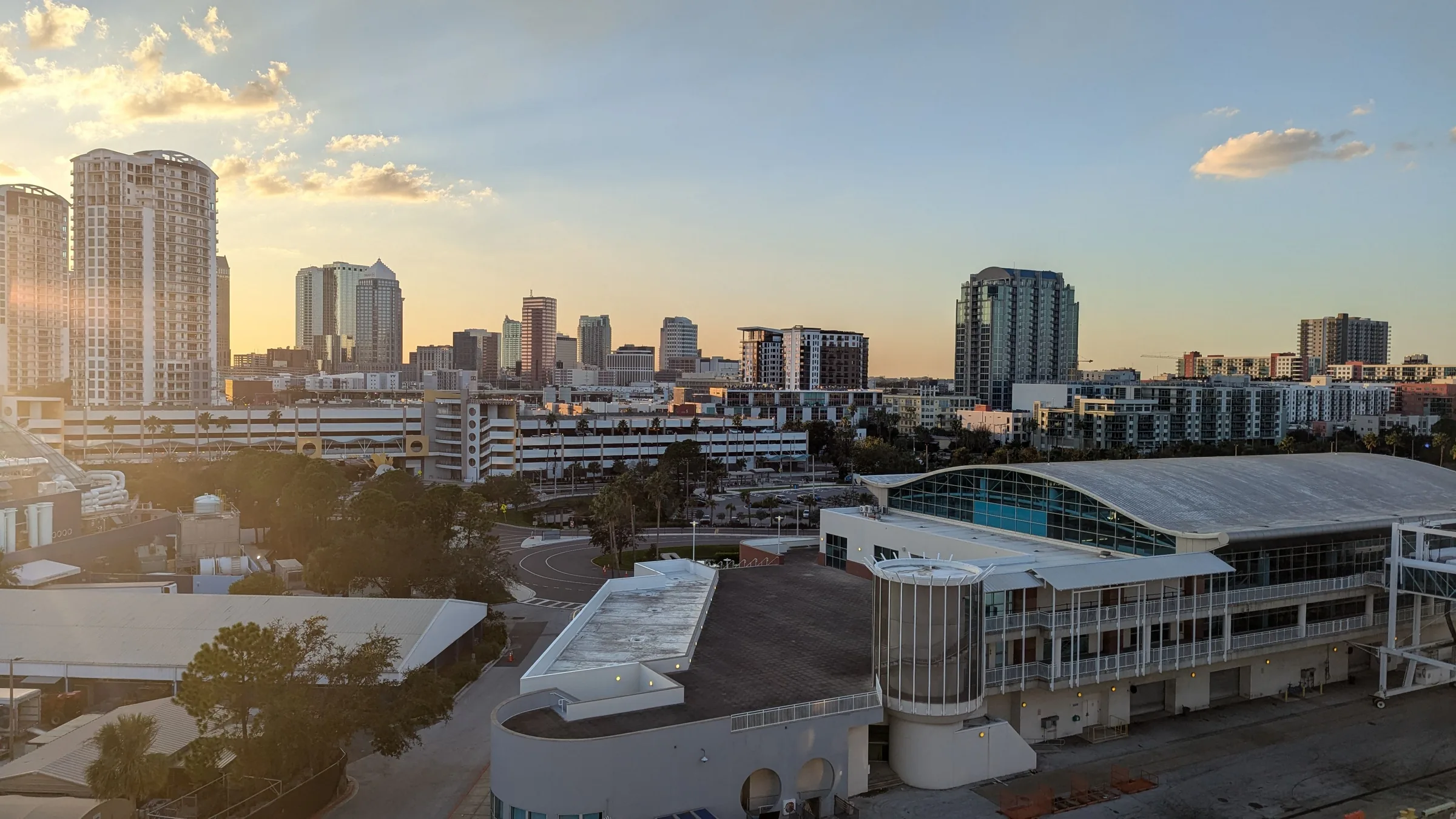 Modern waterfront civic center building with curved glass architecture overlooking a city skyline at sunset.